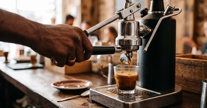 Close-up of hands operating a lever espresso machine group head with a portafilter, in warm atmospheric café lighting